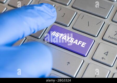 Travail à la maison pendant l'épidémie de virus Corona. Main mâle dans un gant bleu touchant le clavier entrer la clé rester en sécurité. Travail à domicile. Banque D'Images