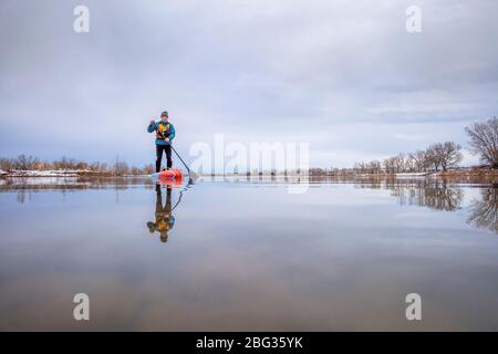 solo lac paddling comme distanciation sociale de loisirs pendant la pandémie de coronavirus, un paddler mâle senior sur stand up paddleboard au début du printemps dans Color Banque D'Images