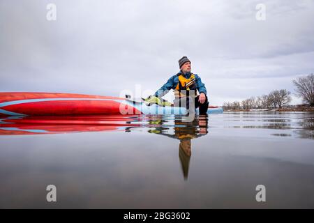 solo lac pagayage comme distanciation sociale de loisirs pendant la pandémie de coronavirus, un paddler mâle senior a un moment de réflexion lorsqu'il est assis sur sa p Banque D'Images