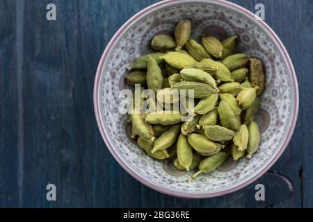 Graines entières de cardamome vert dans un bol vintage sur fond de bois Banque D'Images