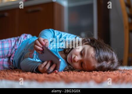 Jolie petite fille heureuse posée sur l'utilisation de smartphone numérique mobile dans le salon à la maison. Concept d'activité familiale. Banque D'Images