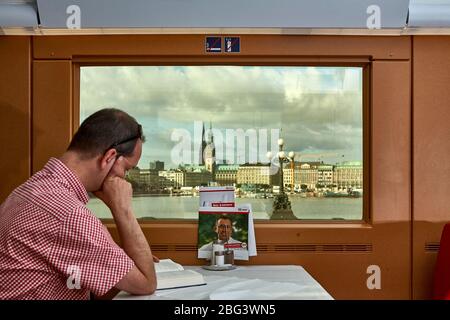 Un passager lisant un livre dans le restaurant car d'un train traversant le pont entre les deux lacs Alster dans le centre de Hambourg avec vue sur Banque D'Images