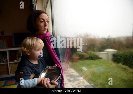 Une jeune mère souffrant de dépression postnatale est assise à une fenêtre avec son enfant Banque D'Images