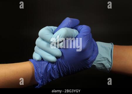 Symbole de la pandémie de coronavirus. Poignée de main protégée par des gants en caoutchouc. Banque D'Images