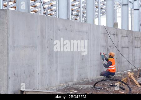 Un travailleur nettoie un mur de béton avec une meuleuse. Préparation d'une surface plane sur un mur de béton après l'installation Banque D'Images