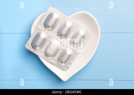 paquet de pilules médicales dans une plaque blanche en forme de coeur sur un bleu de bois. Vue de dessus. Gros plan. Concept contraceptif Banque D'Images