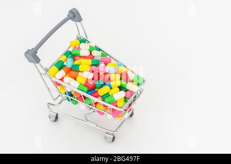 Mini chariot de shopping plein de comprimés colorés caplets. Métaphore Big Pharma, ventes médicales, médicaments en vente libre, hypocondrie / hypocondrie, pénurie de médicaments Banque D'Images