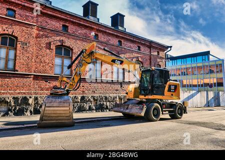 Nouvelle pelle hydraulique sur pneus M315 F Cat stationnée sur une allée à côté du bâtiment historique en brique rouge à partir de la ville de 1889. Helsinki, Finlande. 19 avril 2020. Banque D'Images