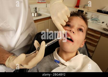 Dentiste l'injection d'un anesthésique local anti douleur dans les gommes d'un jeune avant de commencer la chirurgie dentaire. Banque D'Images