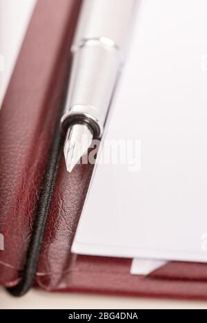 Stylo plume sur un dossier en cuir de luxe ouvert avec des livres blancs prêts à prendre des notes. Banque D'Images