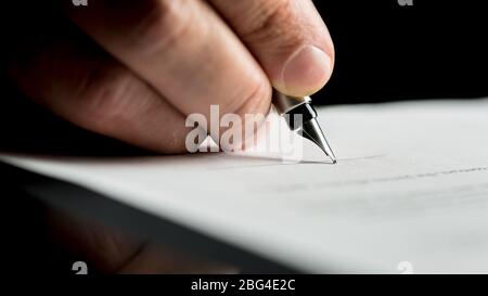 Plan macro sur une main d'un homme d'affaires signature ou l'écriture d'un document sur une feuille de papier blanc à l'aide d'un stylo nibbed. Banque D'Images