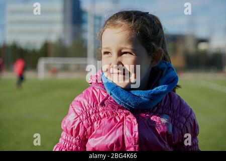 petite fille souriante portant un manteau rose dans un stade de football Banque D'Images