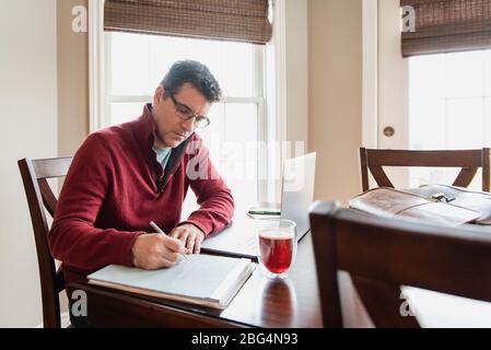 Homme dans des lunettes travaillant à la maison en utilisant un ordinateur à une table à manger. Banque D'Images