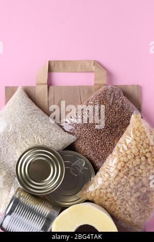 Sac en papier avec fournitures alimentaires crise stock de nourriture pour la période d'isolement de quarantaine sur fond rose. Riz, sarrasin, pâtes alimentaires, conserves alimentaires, papier toilette Banque D'Images