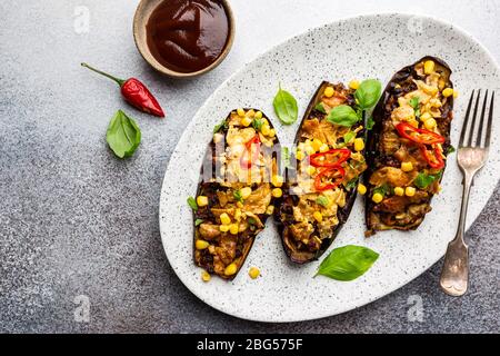 Bateaux d'aubergines cuits au four, farcis de viande hachée, tomates, maïs, ail et fromage en plaque blanche, vue de dessus Banque D'Images