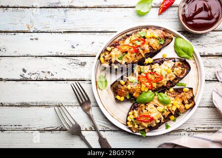 Bateaux d'aubergines cuits au four, farcis de viande hachée, tomates, maïs, ail et fromage en plaque blanche, vue de dessus Banque D'Images