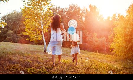 Fête des mères. Petite fille courir avec la mère et tenir des balons dans la main. Famille s'amuser dans le parc d'été Banque D'Images