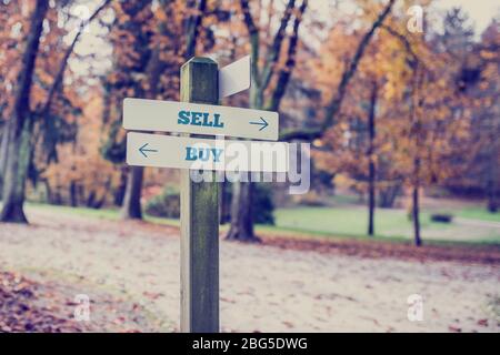 Image rétro d'un panneau de signalisation rural avec deux panneaux disant - Vendre - Acheter - pointant dans des directions opposées. Banque D'Images