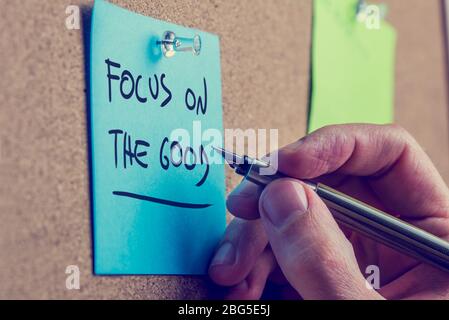 L'homme écrivant un message de motivation sur un tableau de bord de liège sur un mémo bleu disant - Focus sur le bien - se rapprochez de sa main et le marqueur stylo avec le Banque D'Images