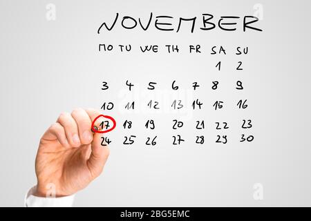 Gros plan de la main d'un homme qui sonnait le 17 novembre sur un calendrier manuscrit sur une interface virtuelle avec un marqueur rouge comme rappel de l'internat Banque D'Images