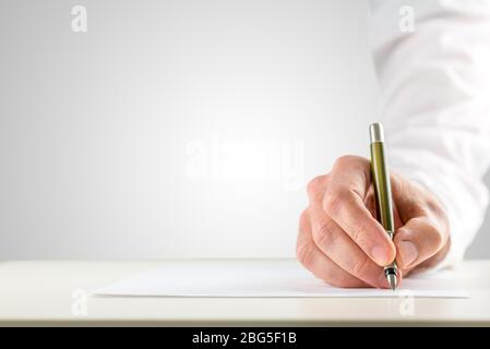 Gros plan d'une main masculine avec manche blanc tenant un point de bille pour commencer à écrire sur un papier vierge placé sur le bureau, avec espace de copie sur le gris b Banque D'Images