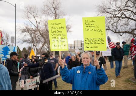 Helena, Montana - 19 avril 2020: Une femme citoyenne senior protestant en tenant des signes d'écriture bible lors d'un rassemblement de prière au Capitole de l'État. Test du Banque D'Images