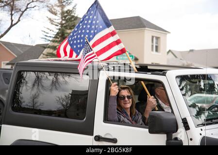 Helena, Montana - 19 avril 2020: L'homme et la femme tiennent des drapeaux américains dans une jeep blanche lors d'un rassemblement de liberté autour de Capitol Square contre la fermeture du gouvernement Banque D'Images