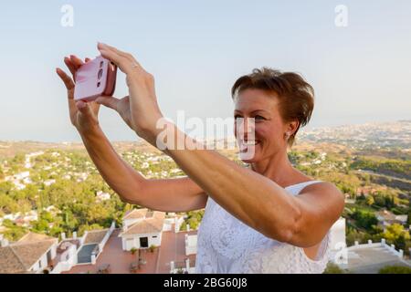 Heureuse femme de tourisme mûre prenant photo avec téléphone du beau paysage du village de Mijas en Espagne Banque D'Images