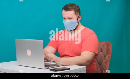 L'homme barbu adulte caucasien travaille à la maison. Photo de concept de style de vie avec espace de copie. Photo avec un gars qui utilise un masque de protection. Banque D'Images
