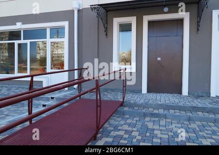 Rampe d'accès pour fauteuils roulants pour l'entrée d'un immeuble résidentiel à plusieurs étages, d'une rue de la ville et d'un trottoir en tuiles Banque D'Images