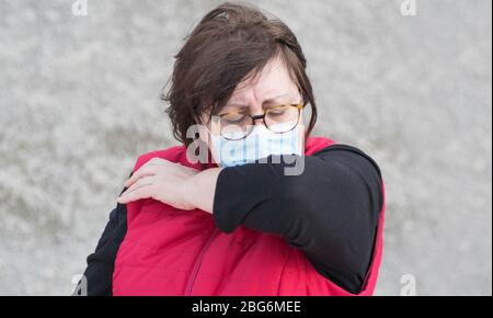 Concept de transmission du virus du coronavirus ou du virus COVID. Une femme dans la rue tousse ou éternuer dans le coude portant un masque de protection à Murcie, en Espagne. Banque D'Images