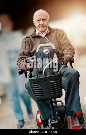 Vieux homme âgé d'âge mûr portant un tube d'oxygène nasal, en conduite sur un scooter de mobilité Banque D'Images