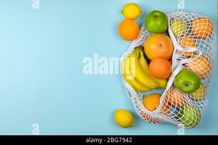 pommes de banane aux fruits oranges citron dans le filet de caton , sac de shopping à cordes sur un fond bleu. concept zéro déchet. Pas de plastique. Banque D'Images