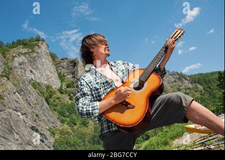 Un touriste masculin joue un rock roll sur une guitare surplombant les montagnes. Plaisir des loisirs en plein air Banque D'Images