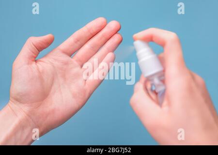 Mains vaporiser du désinfectant pour nettoyer et protéger les mains contre les virus sur fond bleu. Gros plan sur le smartphone désinfectant des mains. Nettoyez les mains avec Banque D'Images