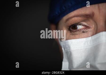 Un médecin ou une infirmière féminine stressée portant un masque facial médical sur fond sombre. Banque D'Images