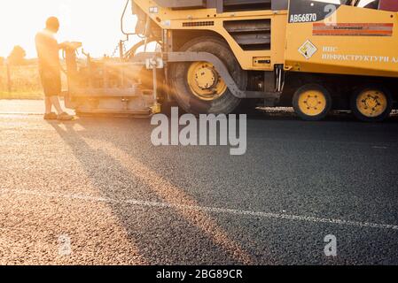 Travailleur routier exploitant une machine à asphalte qui pond de l'asphalte ou du bitume neuf pendant la construction de routes Banque D'Images