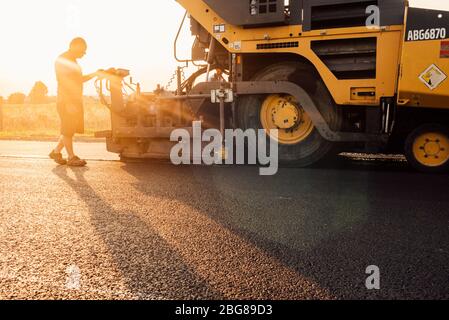 Travailleur routier exploitant une machine à asphalte qui pond de l'asphalte ou du bitume neuf pendant la construction de routes Banque D'Images