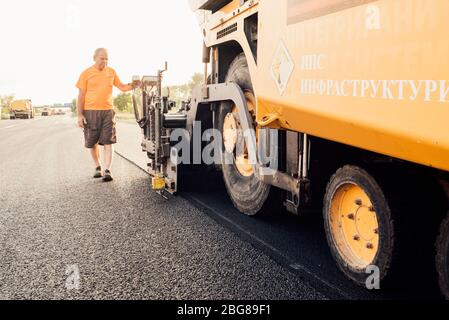 Travailleur routier exploitant une machine à asphalte qui pond de l'asphalte ou du bitume neuf pendant la construction de routes Banque D'Images