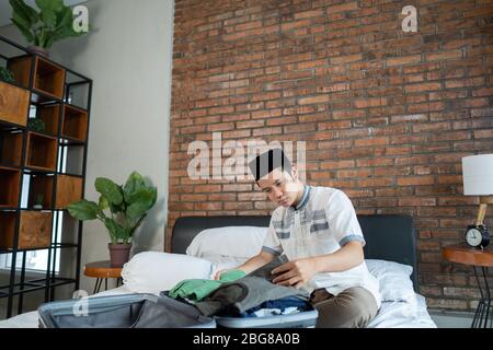 Jeune homme musulman préparant et emballer des vêtements sur le lit à la chambre Banque D'Images