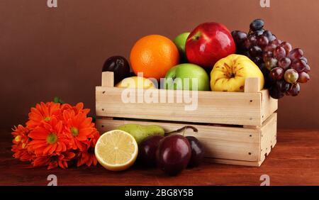 Différents fruits en caisse et fleurs sur table sur fond brun Banque D'Images