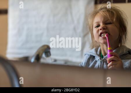 Gros plan émotionnel d'une jolie petite fille se brossant les dents avec une brosse à dents électrique. Banque D'Images