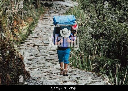 Porter man randonnée sur la piste Inca tout en transportant une charge lourde d'équipement. Banque D'Images