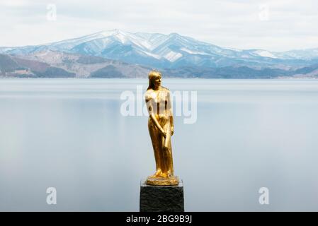 Une statue dorée de Tatsuko se dresse contre la majestueuse eau du lac Tazawa. Banque D'Images