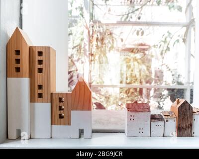 Maisons en bois miniatures sur étagère blanche près de la vitre avec lumière du soleil, restez en sécurité à la maison concept. Banque D'Images