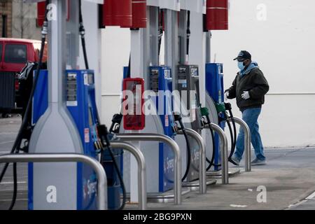 (200421) -- NEW YORK, le 21 avril 2020 (Xinhua) -- un homme portant un masque passe par des pompes à gaz à une station-service du quartier de Brooklyn, à New York, aux États-Unis, le 20 avril 2020. Les prix du pétrole américain ont été écrasés sur le territoire négatif pour la première fois dans l'histoire lundi, alimentés par un choc de la demande et des craintes de suroffre liées à la pandémie. Le West Texas Intermediate (WTI) pour la livraison de mai a versé 55,9 dollars américains, ou plus de 305 pour cent, pour régler à -37,63 dollars le baril sur le New York Mercantile Exchange, ce qui implique que les producteurs paieraient aux acheteurs de retirer le pétrole de leurs mains. (Photo de Michae Banque D'Images