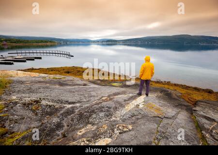 Vue panoramique sur le fjord. Le jeune homme debout sur la roche et regardant la mer. Magnifique paysage de montagne au coucher du soleil. Nature scandinave. N Banque D'Images