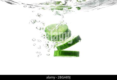 Chute de tranches de concombre frais dans l'eau sur fond blanc Banque D'Images