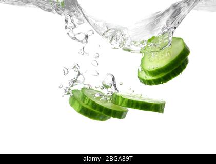 Chute de tranches de concombre frais dans l'eau sur fond blanc Banque D'Images