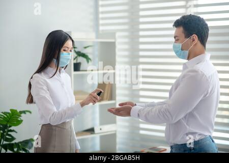 Femme embauchée dans un noir tenant un désinfectant et le vaporisant sur la main Banque D'Images